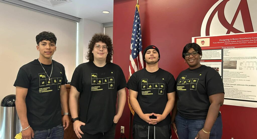 Four students in black t-shirts pose for a photo in front of a research poster